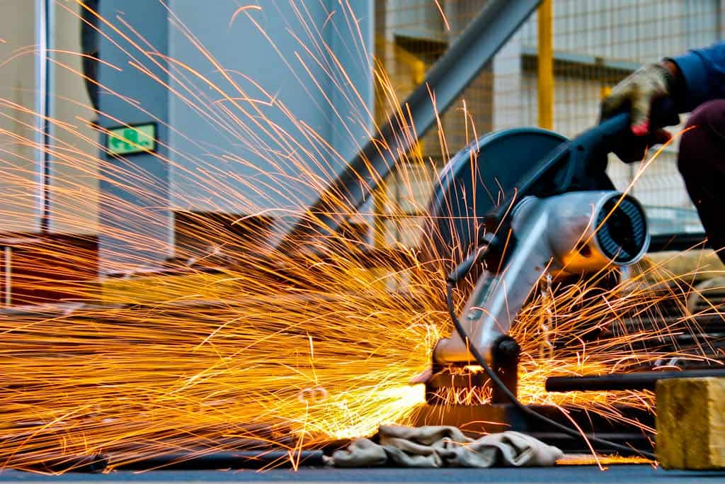 A worker operates a grinder cutting metal, creating a vibrant display of sparks in an industrial setting,, which sets context for advocating for the productivity commission.