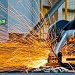 A worker operates a grinder cutting metal, creating a vibrant display of sparks in an industrial setting,, which sets context for advocating for the productivity commission.