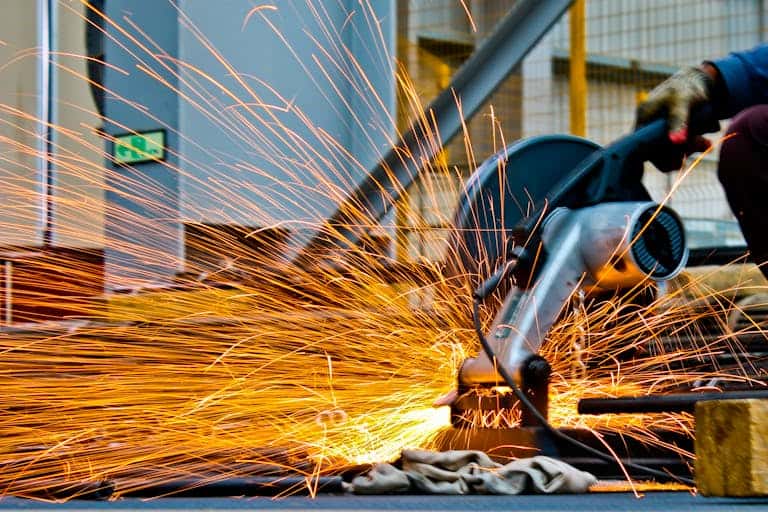 A worker operates a grinder cutting metal, creating a vibrant display of sparks in an industrial setting,, which sets context for advocating for the productivity commission.