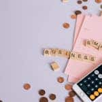 Flat lay of a small business payroll tax planning scene with coins, smartphone calculator, and letter tiles.