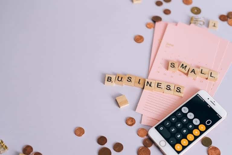 Flat lay of a small business payroll tax planning scene with coins, smartphone calculator, and letter tiles.